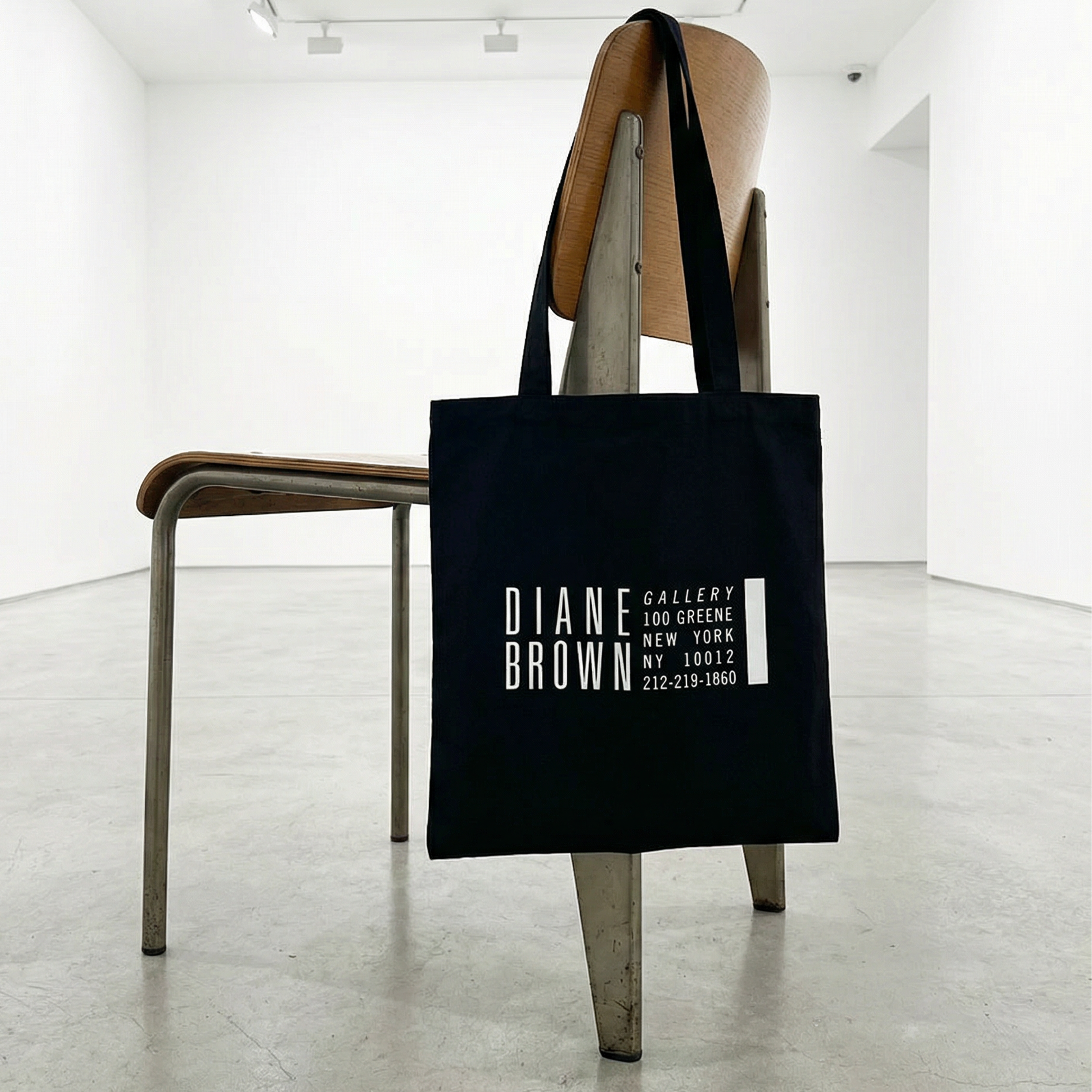 Black tote bag with text hanging on a chair in a minimalistic room